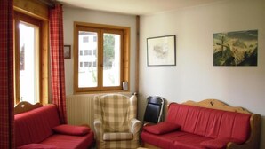 Una sala de estar acogedora con un sofá rojo, un sillón estampado, una mesa de centro de madera y un radiador.