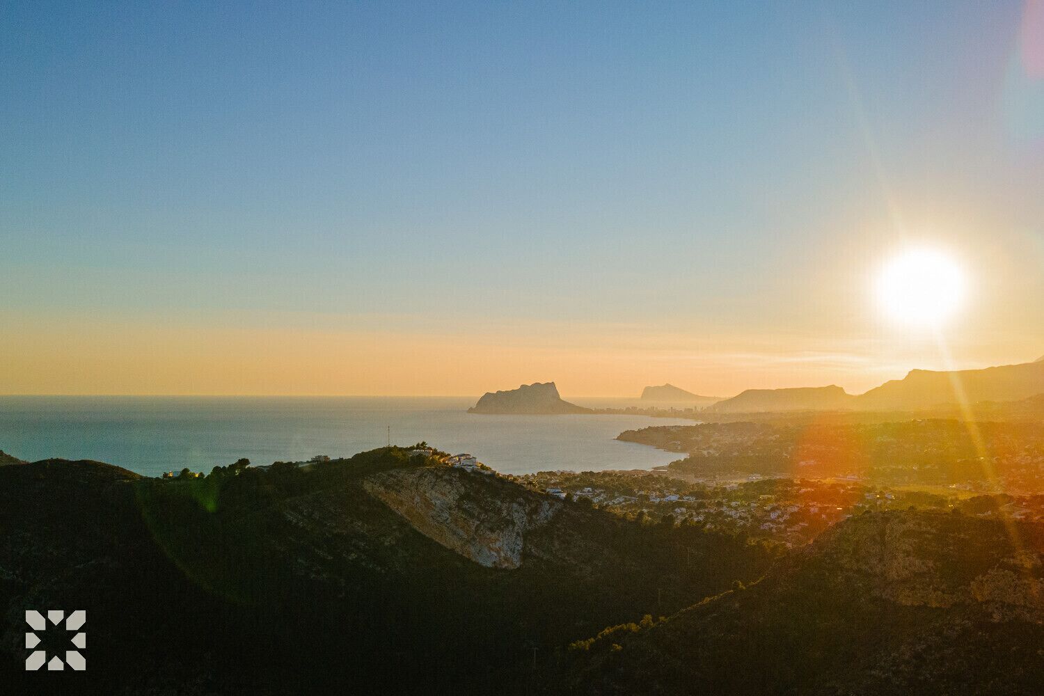 Un paisaje costero con amanecer o atardecer, colinas y una masa de agua.