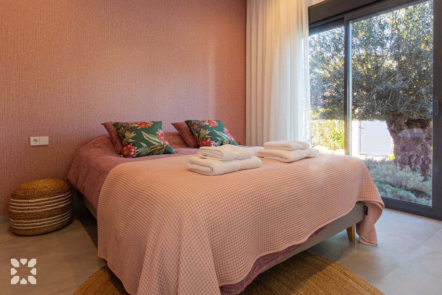Une chambre à coucher avec un grand lit, deux oreillers, une table de chevet et une vue sur les arbres par la fenêtre.