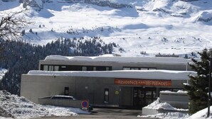 A building labeled "Residence Les Pleiades" with a parking area and snow-covered mountains in the background. - 150m from shops, 2nd floor, balcony, tv, ski locker, 40m², Flaine (Flaine)