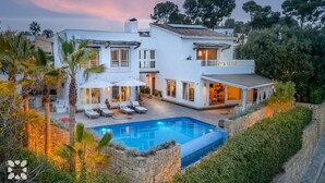 Una casa de dos pisos con piscina, mobiliario exterior y un muro de contención de piedra.
