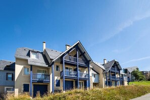 Uma fileira de casas geminadas modernas, com dois andares e varandas, em uma área gramada e ensolarada.