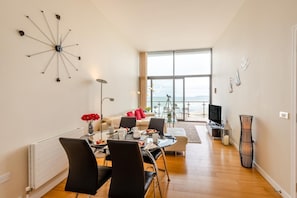 A modern living room with a dining area, large windows, and a view of the sea.
