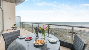 Un balcon avec une table dressée pour le dîner, donnant sur une plage rocheuse.
