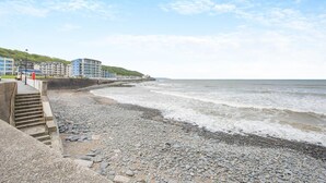 Un hôtel situé sur la côte, doté d’une plage de galets, d’un escalier menant à la plage et de bâtiments avec des balcons donnant sur la mer.
