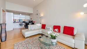 Ein modernes Wohnzimmer mit einem Ecksofa, einem Glastisch und einer Küche im Hintergrund.