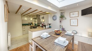 Una cucina moderna con un lucernario, una zona pranzo con tavolo in legno e una TV a parete.