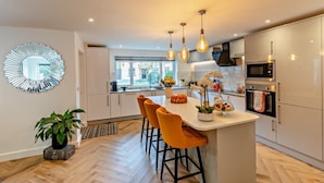 Une cuisine moderne dotée d’un îlot central, de luminaires suspendus et offrant une vue sur l’extérieur.