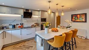 Une cuisine moderne avec des armoires blanches, un comptoir en marbre et des luminaires suspendus. On y trouve également un coin repas avec des chaises jaunes et une table blanche.