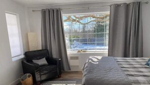 Un dormitorio con cama, una silla, una ventana con cortinas y vistas al exterior.