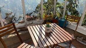 Un conjunto de mesa y sillas de madera en una habitación soleada con ventanas amplias, una planta en maceta y una silla azul.