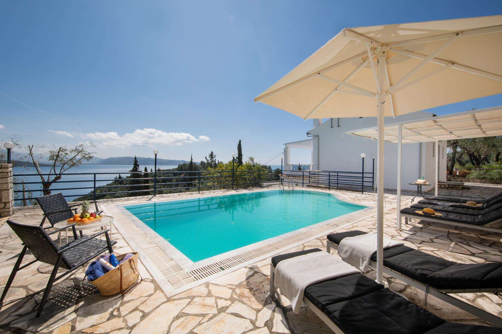 Ein Poolbereich mit Liegestühlen, einem Tisch mit Früchten und Blick aufs Meer.