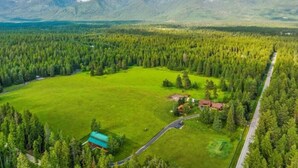 Eine Luftaufnahme eines ländlichen Anwesens mit einem großen grünen Feld, einem kleinen Haus mit rotem Dach und einer Straße.