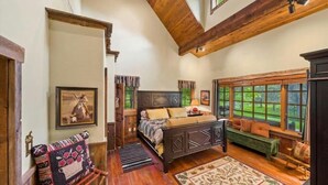 A cozy bedroom with a large bed, a bench, and a view of the outdoors through a window. - G-Bar-N Ranch Pendleton Log Home (Bigfork)
