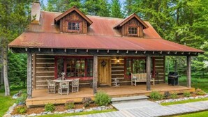 A rustic log cabin with a porch, two chimneys, and a small deck area. - G-Bar-N Ranch Pendleton Log Home (Bigfork)