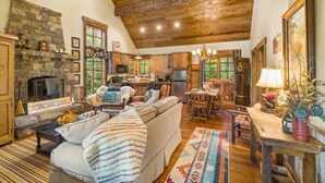 A rustic cabin interior with a stone fireplace, wooden ceiling, and a cozy living area with a sofa and dining table. - G-Bar-N Ranch Pendleton Log Home (Bigfork)