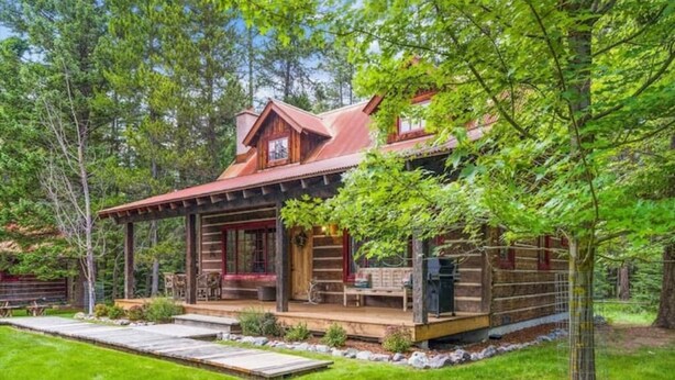 A rustic cabin with a covered porch, a fireplace, and a well-maintained lawn. - G-Bar-N Ranch Pendleton Log Home (Bigfork)