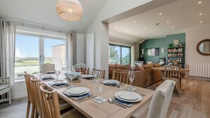 Un coin repas avec une grande table dressée pour six personnes, un luminaire suspendu et une vue sur l’extérieur.