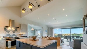 Une cuisine moderne dotée d’un îlot central, un coin repas avec vue et un espace de vie comprenant un canapé et des fauteuils.