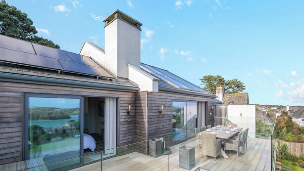 Une maison moderne dotée d’une terrasse, de grandes fenêtres et de panneaux solaires.
