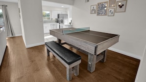 Une table de billard dans une pièce dont le sol est en bois, avec un banc et un luminaire au plafond.