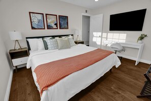 Une chambre à coucher avec un grand lit, un bureau, une chaise, un téléviseur et des œuvres d’art accrochées au mur.