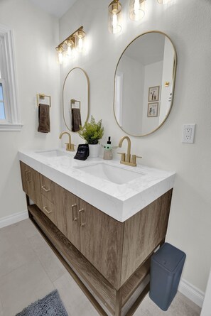 Une salle de bain dotée d’un meuble-lavabo à deux vasques, de meubles en bois, d’un grand miroir et d’un éclairage mural.