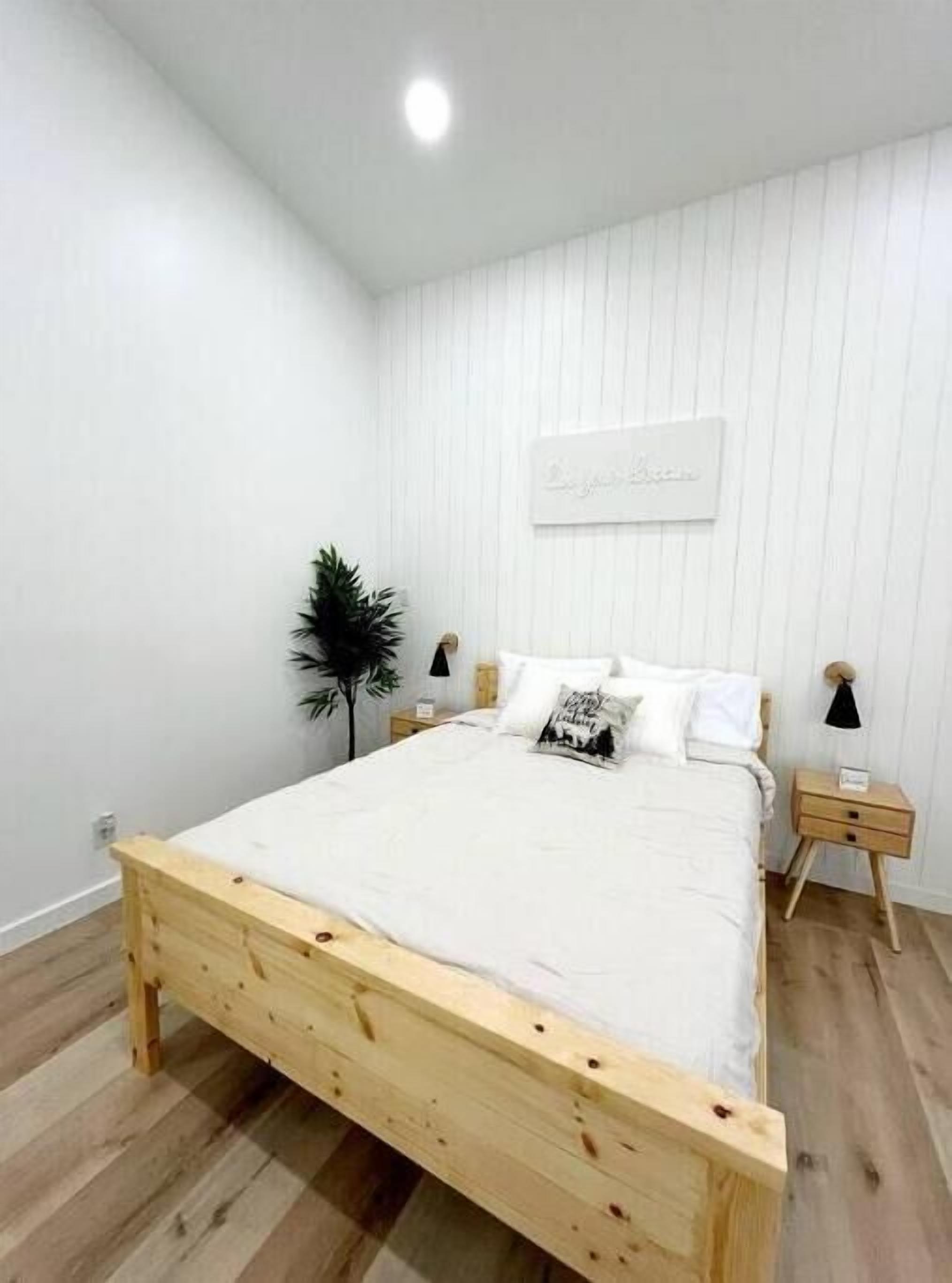 A minimalist bedroom with a wooden bed, white walls, and a small bedside table.
