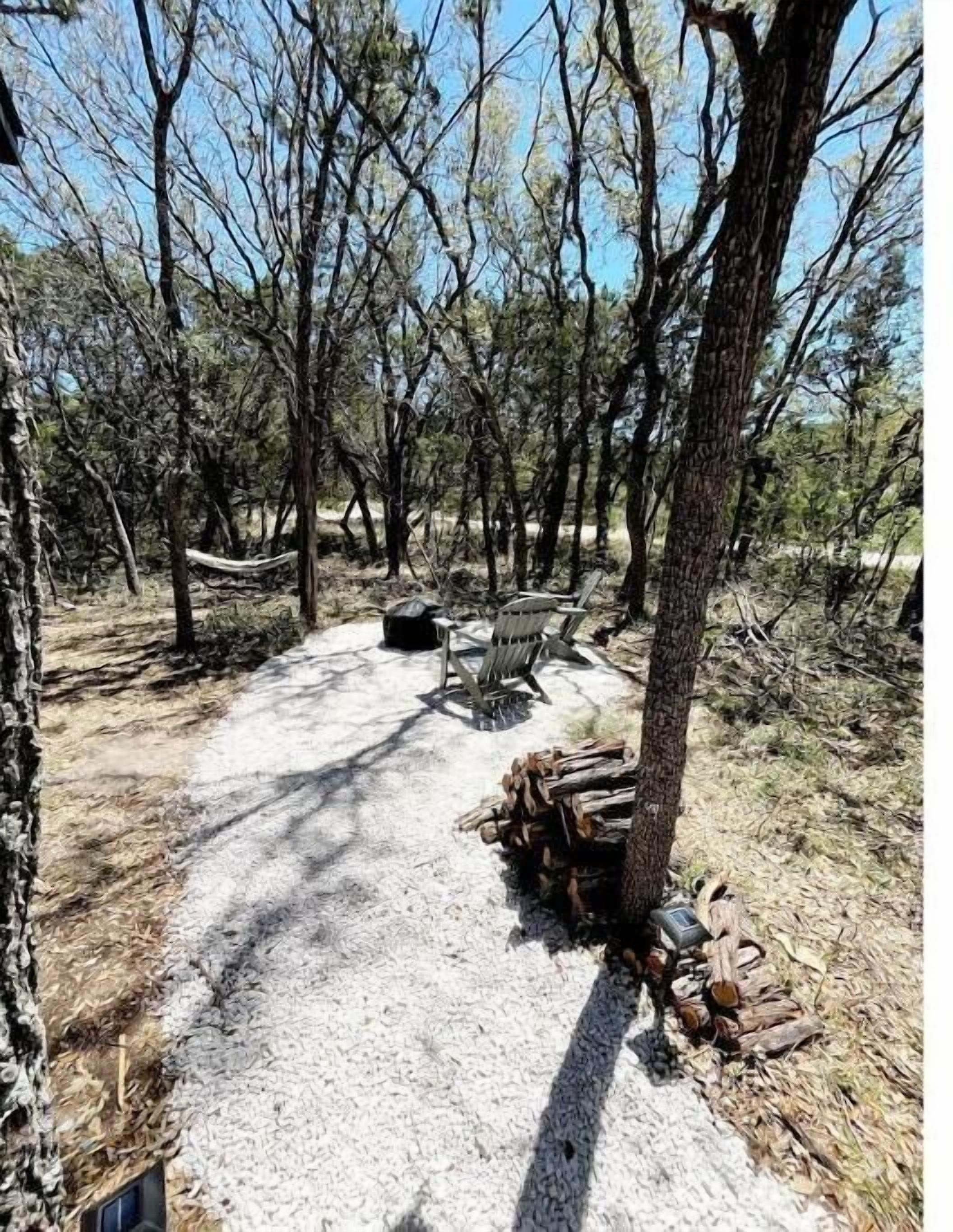 A campsite with a gravel path leading to a fire pit, surrounded by trees and a hammock.