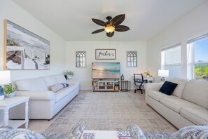 A living room with a ceiling fan, a TV, a bookshelf, and a painting of a beach scene.