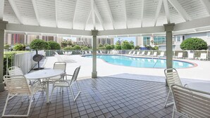Ein überdachter Poolbereich mit Liegestühlen und einem Tisch, umgeben von einem weißen Zaun und Grünpflanzen.