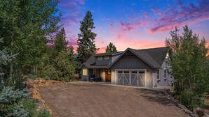 Une maison à deux étages avec un garage, entourée d’arbres et bordée d’une allée en gravier.