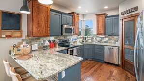 Une cuisine dotée de plans de travail en granit, de meubles en bois, d’appareils électroménagers en acier inoxydable et offrant une vue sur Aspen Avenue.