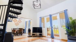 A spacious living room with a staircase, a flat-screen TV, and a dining area. - Golden Dream Villas & Studio A/B Poll View (Isabela)