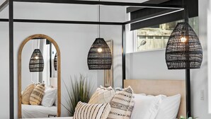 Un dormitorio moderno con una cama, dos lámparas colgantes, un espejo grande y una ventana.