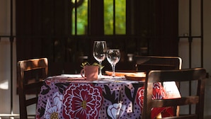 A table with a floral tablecloth, two wine glasses, a small potted plant, and a wooden chair with a red cushion. - Casona El Resguardo (San Esteban)