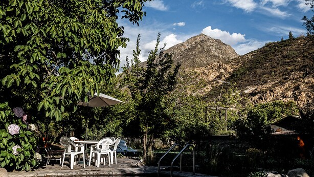 A serene outdoor seating area with a table and chairs, a small bridge over a calm water body, and a mountain in the background. - Casona El Resguardo (San Esteban)