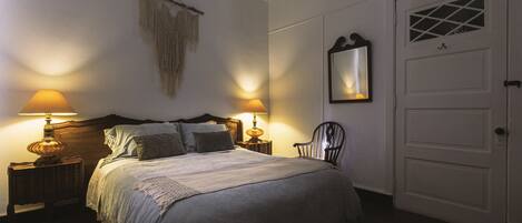 A neatly made bed with a headboard, two bedside lamps, a decorative wall hanging, and a door with a window.