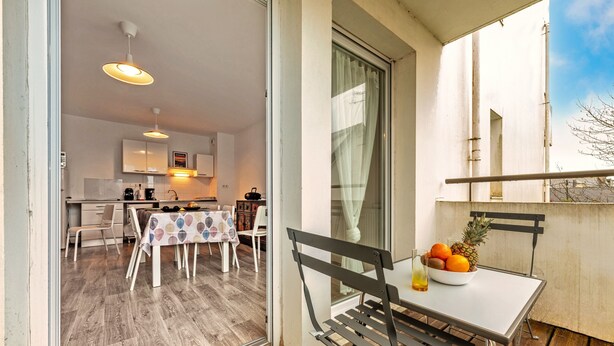A balcony with a table, a bowl of fruit, and a bottle of juice.