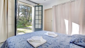 A bedroom with a large bed, two towels, a window with curtains, and a door leading outside. - Sarah 3 - Appt à avec jardin à 200 m de la plage (Fréhel)