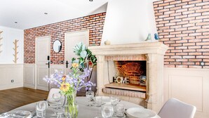 A dining area with a brick wall, a fireplace, and a table set for six with clear glassware and white plates. - Sarah 3 - Appt à avec jardin à 200 m de la plage (Fréhel)