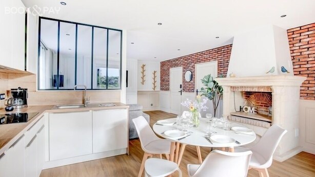 A modern kitchen with a central island, white cabinetry, and a large window. - Sarah 3 - Appt à avec jardin à 200 m de la plage (Fréhel)