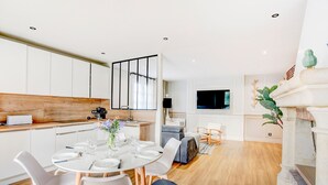 A modern kitchen with white cabinets, a wooden countertop, and a dining area with a round table and chairs. - Sarah 3 - Appt à avec jardin à 200 m de la plage (Fréhel)