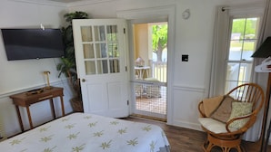 Et soveværelse med seng, fjernsyn, dør til en balkon og en fletstol.