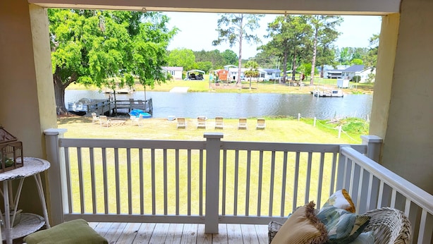 En veranda med fletmøbler og udsigt over en sø med både og huse i baggrunden.