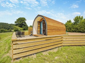 A wooden dome-shaped building with a door, a patio with chairs, and a wooden deck. - Rabbits Rest - UK46128 (Nesscliffe)