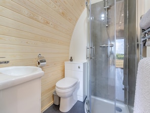 A bathroom with a wooden wall, a toilet, a sink, and a glass-enclosed shower.