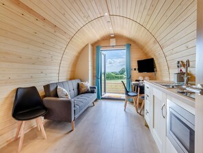 A cozy, curved-roofed room with a sofa, chairs, a dining table, and a kitchen area.