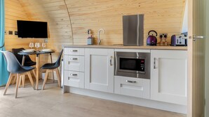 Cuina compacta amb microones, teixidor i torradora, sostre de fusta i zona de dinar amb cadira i taula.