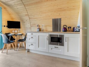 Cozinha compacta com micro-ondas, chaleira e torradeira, teto de madeira e área de jantar com cadeiras e mesa.